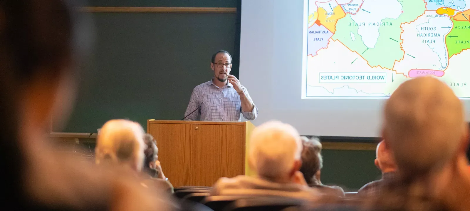 Professor next to map speaking to seated audience